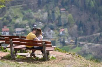 A guy and a girl are sitting on a bench on top of a mountain and admiring the beautiful European landscape.