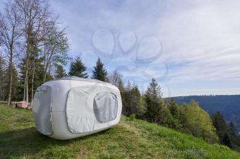 Unusual tent in the form of a cube for outdoor recreation or sleep, set on the mountainside next to the forest