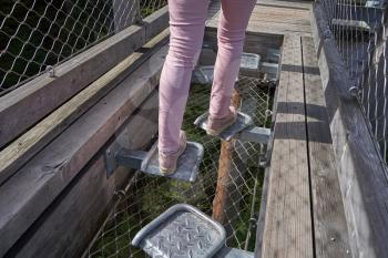 Tourist girl runs on a wooden bridge with entertainment, transparent floor on a bridge in the German forest