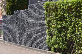 Gabion fence, made of durable mesh and large stones. European fence of mesh and stones