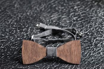 Stylish men's brown wooden bow tie with gray fabric on an iron rough surface. Accessory for brutal men, close up