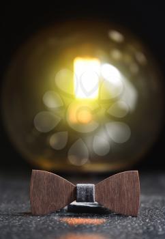 Stylish men's brown wooden bow tie with gray fabric on an iron rough surface and a retro lamp glowing on the background.