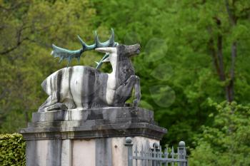 Stone statue of a lying deer with horns on a background of trees, with text space