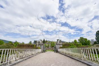 A beautiful white iron bridge in front of the entrance to a public park in the European city of Baden Baden. Landscape with a bridge overlooking a green park