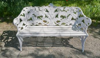 Beautiful white iron bench in a spring park on a background of grass