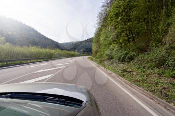 Photo from the window of a car that rides on a road with turns along the forest Schwarzwald. Car hood and forest road