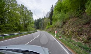 Photo from the window of a car that rides on a road with turns along the forest Schwarzwald. Car hood and forest road