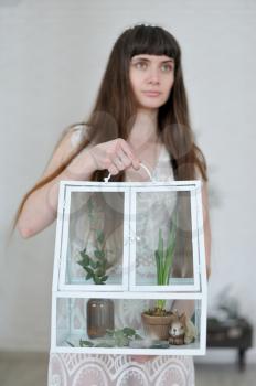 Photo of a young girl in the style of fine art, her hand is holding a large glass florarium inside which are plants and a bunny figure.