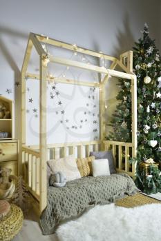 Beautiful children's playroom with wooden furniture, a house decorated for the New Year holiday with a Christmas tree and gifts.