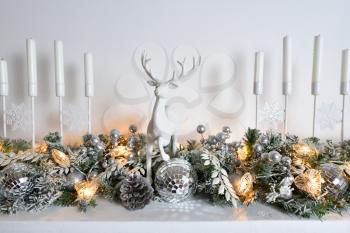 A white deer figurine stands on a fireplace decorated for Christmas or New Year.