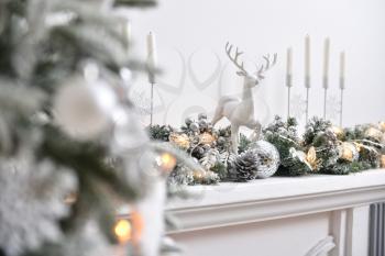 A white deer figurine stands on a fireplace decorated for Christmas or New Year.
