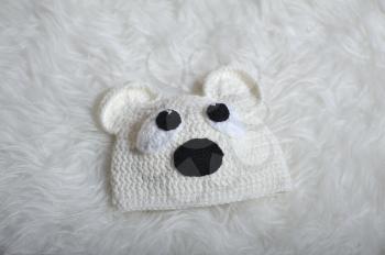Cute children's knitted hat in the form of a teddy bear on a white carpet background