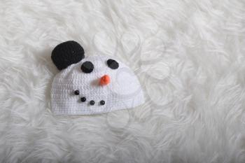 Cute children's knitted hat in the form of a snowman's head on a white carpet background