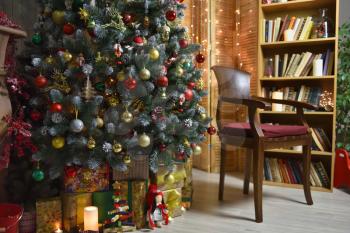 Interior with a decorated Christmas tree, gifts, a wooden armchair and a bookcase with books.