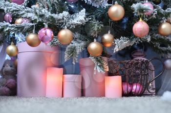 Round boxes and electric candles stand under a snowy Christmas tree on the floor