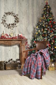 Beautiful Christmas interior in brown tones with a Christmas tree, a fireplace made of wood and a chair with a blanket
