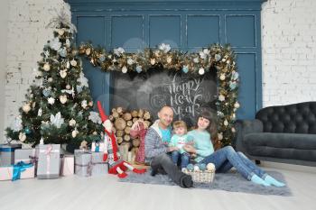 Family dad mom and daughter sit on the carpet and have fun on the background of Christmas decor, chalk inscription happy new year, Christmas tree and gifts