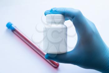 Doctor in blue disposable latex gloves holds a jar of antiviral drugs.