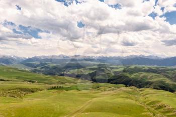 Mountain peaks and grassland are under white clouds. Shot in Xinjiang, China.