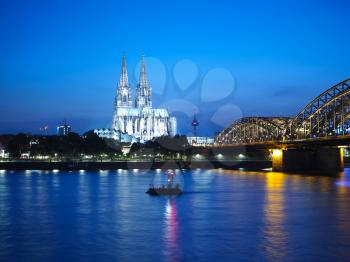 Koelner Dom Sankt Petrus (meaning St Peter Cathedral) gothic church and Hohenzollernbruecke (meaning Hohenzollern Bridge) crossing the river Rhein at night in Koeln, Germany