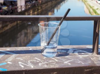A glass of alcoholic cocktail drink on a bridge at Naviglio Grande canal waterway which is the main nightlife place in Milan Italy - focus on glass, with blurred background