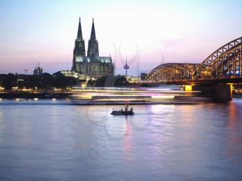Koelner Dom Sankt Petrus (meaning St Peter Cathedral) gothic church and Hohenzollernbruecke (meaning Hohenzollern Bridge) crossing the river Rhein at night in Koeln, Germany