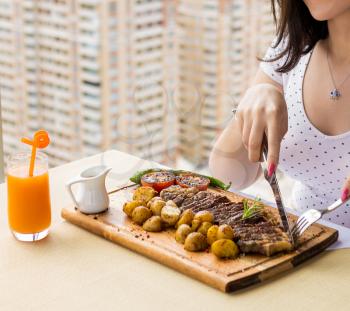 Woman eating tasty steak potato, vegetable on the wood plate