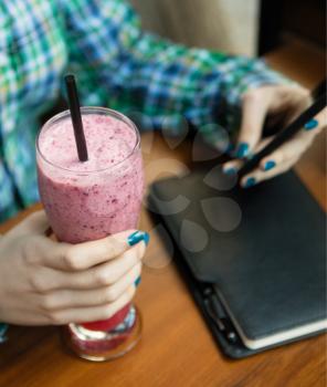 Woman holding cold strawberry milky cocktail, using smartphone