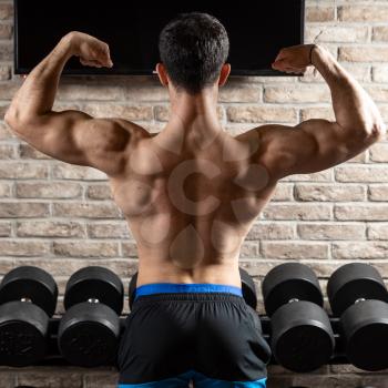 Strong athletic man fitness model posing back muscles, triceps at gym