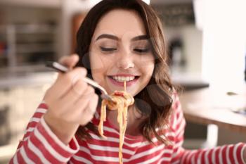 Young woman eating tasty pasta at home�