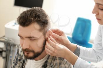 Otolaryngologist putting hearing aid in man's ear in hospital�