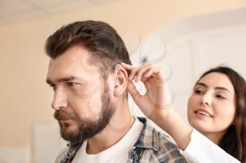 Otolaryngologist putting hearing aid in man's ear on light background�