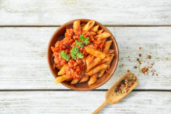 Bowl with tasty penne pasta and bolognese sauce on wooden table�