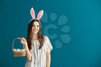 Beautiful young woman with Easter eggs and bunny ears on color background�