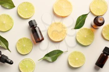 Bottles of essential oils and citrus slices on light background, top view�