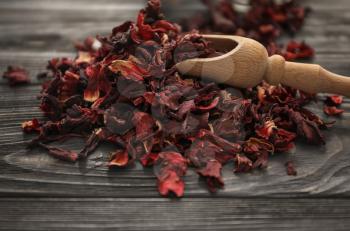 Heap of dry hibiscus tea with wooden scoop on table�