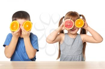 Cute little children with citrus fruits at table on white background�