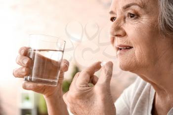 Elderly woman taking pill at home�