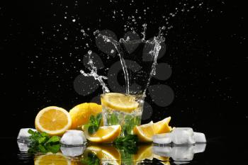 Glass with splashing water and slices of lemon on black background�