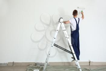 Male painter using roller for refurbishing color of wall indoors�