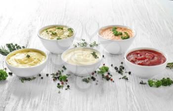 Different tasty sauces in bowls with spices on white wooden table�