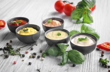 Different tasty sauces in bowls with spices on light wooden table�