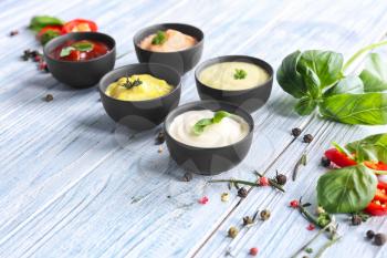 Different tasty sauces in bowls with spices on light wooden table�