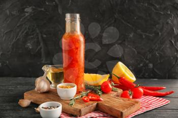 Bottle with tasty sauce, vegetables and condiments on table�