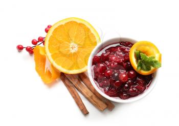 Bowl with tasty cranberry sauce, orange and cinnamon sticks on white background�