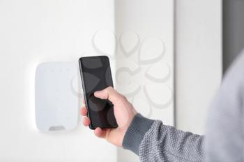 Young man setting alarm system with mobile phone, indoors�