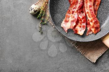 Frying pan with tasty bacon on grey background�