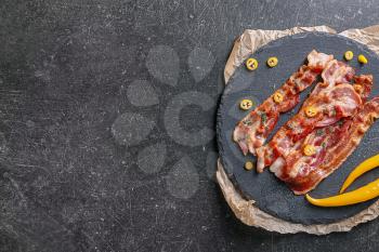Slate plate with tasty fried bacon on dark background�