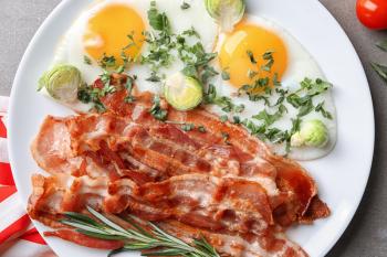 Plate with tasty bacon and fried eggs on table�