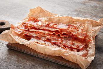 Parchment with tasty fried bacon on wooden board�